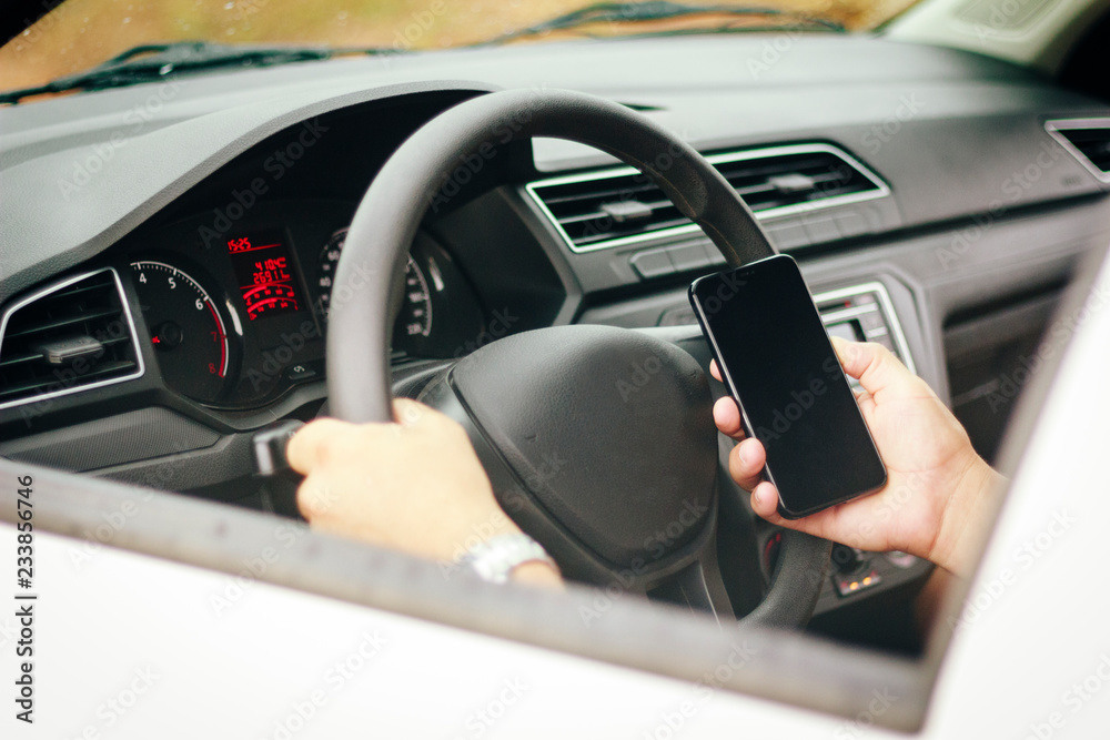 Driver with a hand on the wheel of the car and holding cell phone