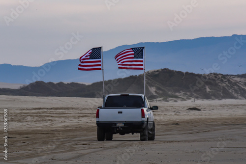 Truck with American flags driving on the beach at dusk.