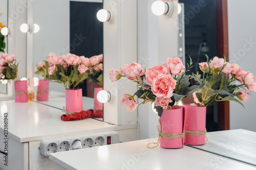 Square mirror with lamps and rose bouquet on visagist working place