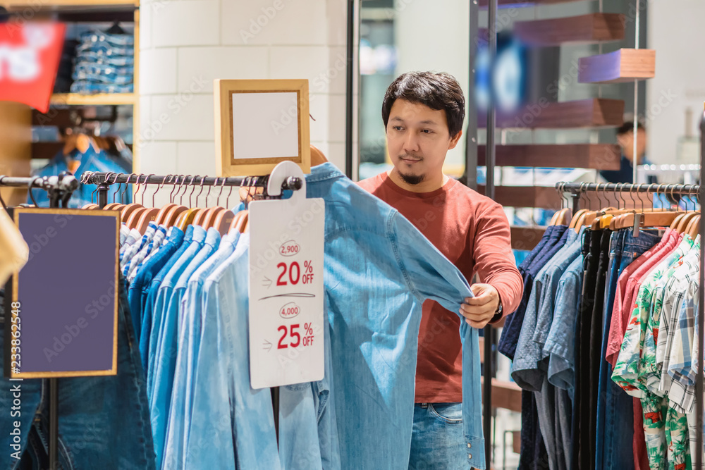 Smart asian man with beard choosing clothes in clothing store at shopping  center, looking white jeans shirts , Fashion and Consumerism Concept. Stock  Photo