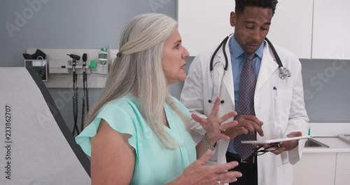 Lovely senior woman explaining to young doctor her chest pain. Black millennial doctor using high tech tablet device indoors health clinic photo