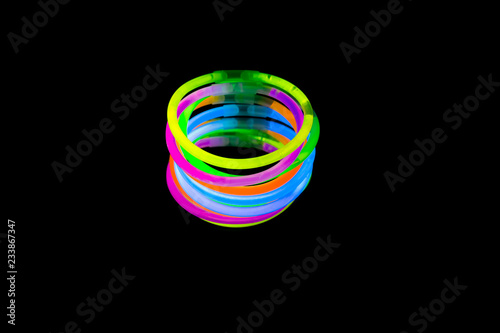 Colorful fluorescent light neon glow stick bracelet strap wristband on mirror reflection black background photo