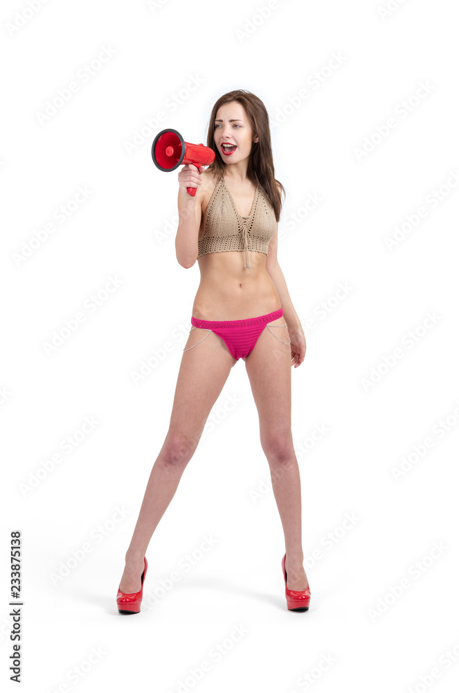 Young happy girl in a swimsuit in red heels with a megaphone. Isolated on white background Young happy girl in a swimsuit in red heels with a megaphone. Isolated on white background