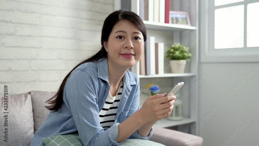 elegant woman face to camera joyfully because of the christmas bargain sale. young asian girl love shopping online at home lifestyle concept. female shopper sit in living room buying by mobile phone. elegant woman face to camera joyfully because of the christmas bargain sale. young asian girl love shopping online at home lifestyle concept. female shopper sit in living room buying by mobile phone.
