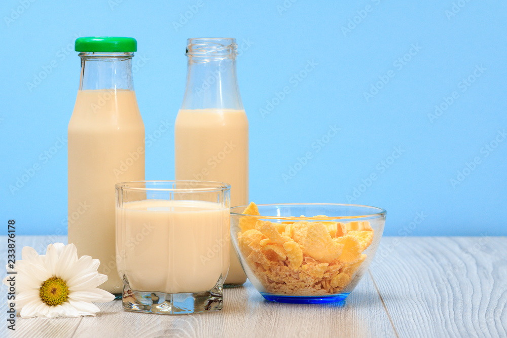 Two bottles and glass of milk, bowl with cornflakes in blue background. Two bottles and glass of milk, bowl with cornflakes in blue background.