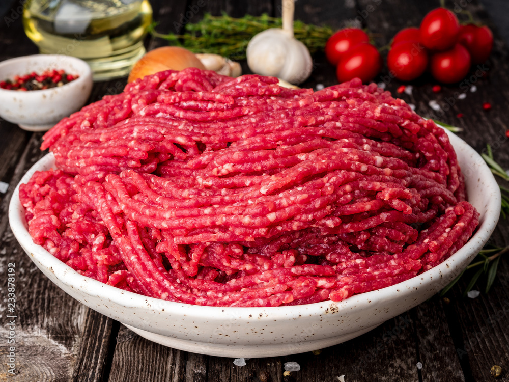 Mince beef, ground meat with ingredients for cooking on old gray dark wooden rustic table, side view