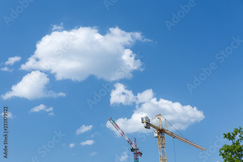 Two tower cranes against a sunny sky with white clouds.