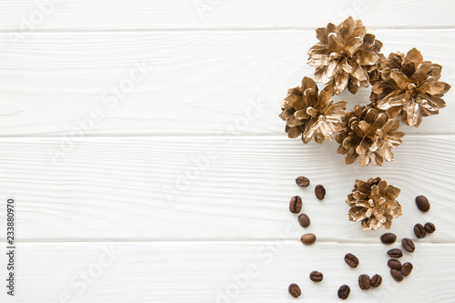 Golden pine cones on white wooden table. Coffee beans decoration. Space for Christmas greeting.