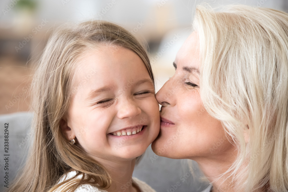 Loving old aged grandmother kissing cute preschool granddaughter on cheek, smiling grandchild girl enjoying care of happy senior mature grandma, two generations granny and kid warm relations Loving old aged grandmother kissing cute preschool granddaughter on cheek, smiling grandchild girl enjoying care of happy senior mature grandma, two generations granny and kid warm relations