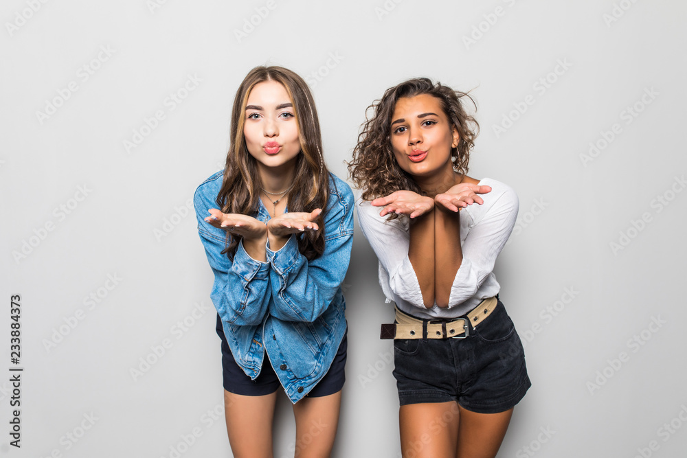 Two multiethnic girls blow airkiss at camera, wears trendy shades, summer clothing, express love or say goodbye on distance, pose against gray background. People, style and diversity concept Two multiethnic girls blow airkiss at camera, wears trendy shades, summer clothing, express love or say goodbye on distance, pose against gray background. People, style and diversity concept