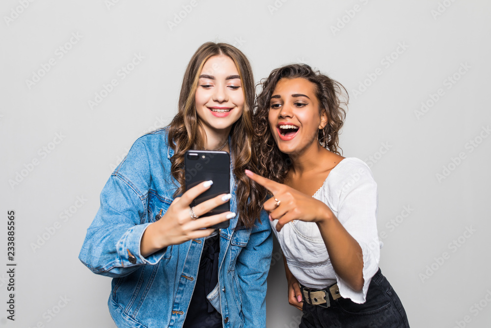 Two cheerful young mixed race girl holding mobile phone while having a video chat isolated over gray background