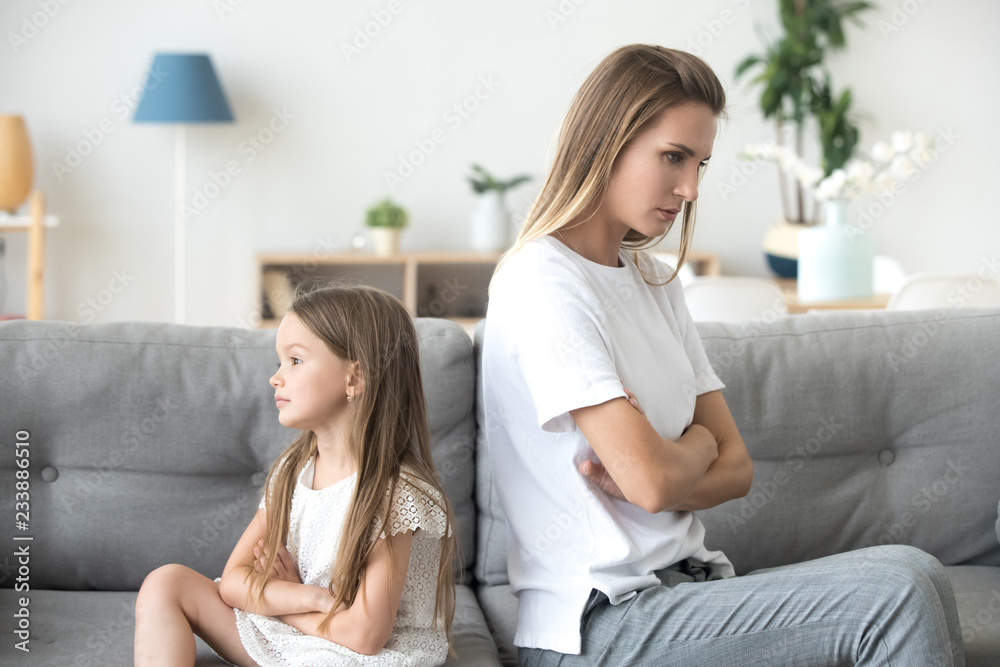 Angry mother and little child girl sitting back to back on sofa not ...