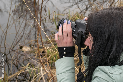 A girl in a warm jacket in the spring photographs objects near the pond