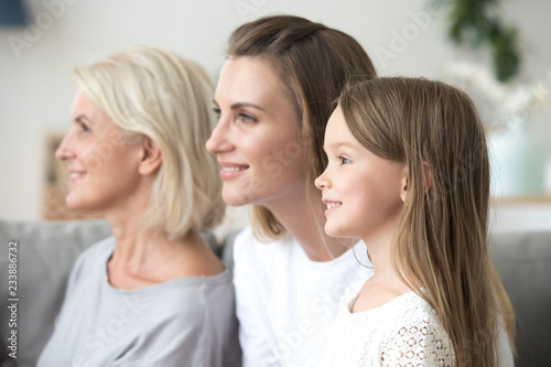 Smiling beautiful women in three generation family looking forward thinking of bright future, happy grandmother young mother and little child daughter dream of good, growing up, aging process concept