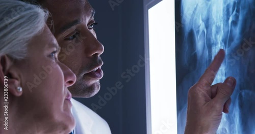 Close view of young male doctor and senior colleague looking at x-ray of patients spine. Close up of millennial black doctor consulting with senior colleague over x ray of spinal bones
