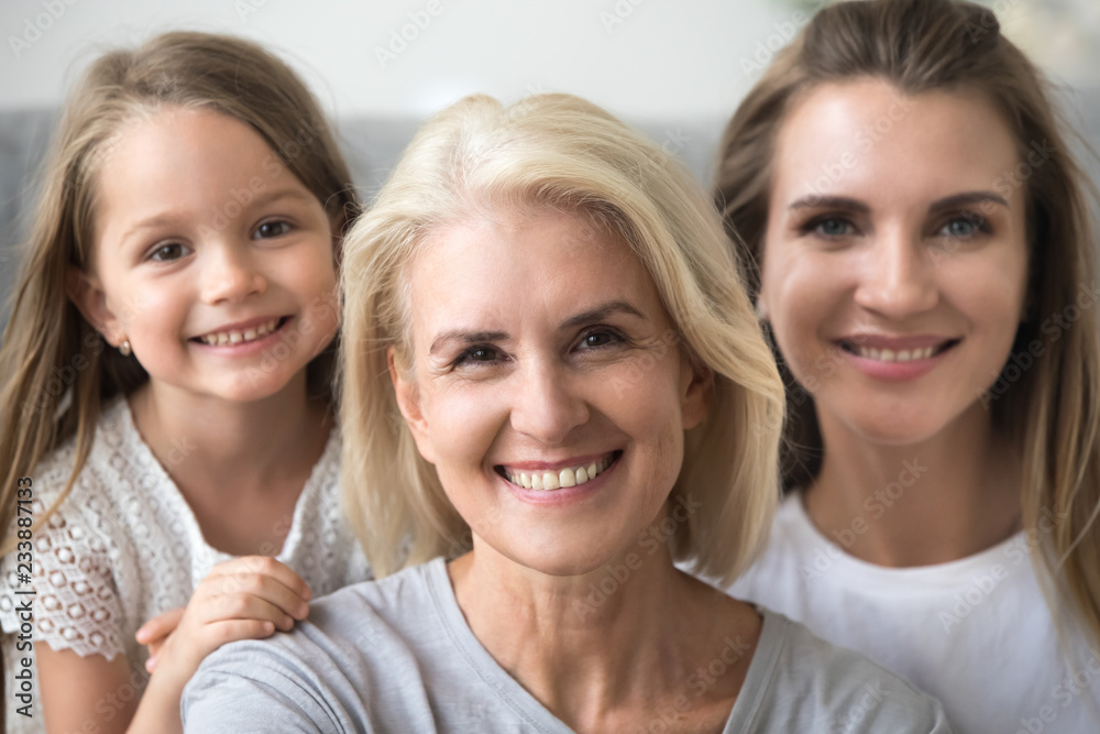 Smiling senior grandmother looking at camera with young daughter and kid granddaughter at background, older grandma in three 3 women happy loving family, older elderly generation concept, portrait Smiling senior grandmother looking at camera with young daughter and kid granddaughter at background, older grandma in three 3 women happy loving family, older elderly generation concept, portrait