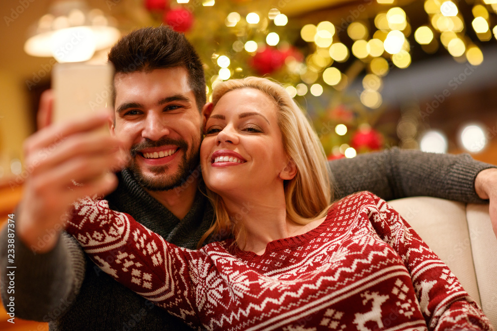 couple in warm sweaters taking selfie picture with smartphone at home.