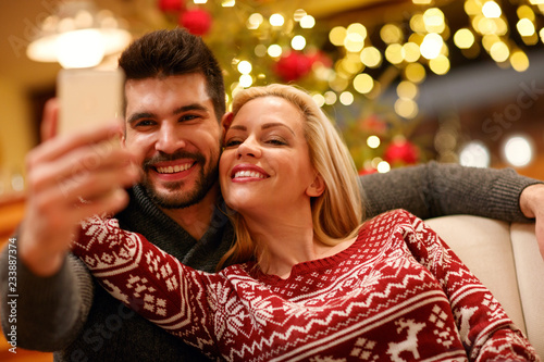 couple in warm sweaters taking selfie picture with smartphone at home.