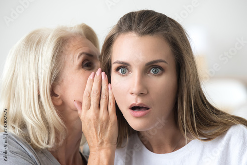 Konstfotografi Old mother whispering in ear of adult daughter telling secret or unbelievable ne