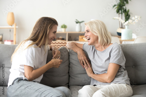 Cheerful old mother and young adult woman talking laughing together, smiling elderly older mum having fun chatting with grown daughter, two age generations pleasant conversation at home concept photo