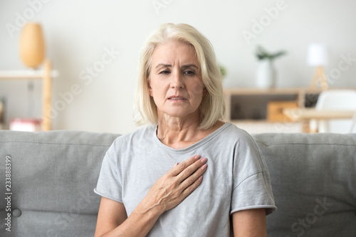 Fototapeta Upset stressed mature middle aged woman feeling pain ache touching chest having