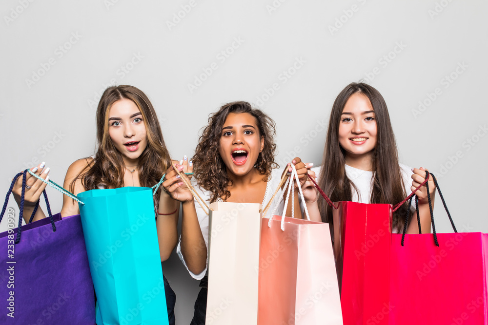 Black friday concept. Portrait of funky positive three mixed race having many colorful bags isolated on gray background Black friday concept. Portrait of funky positive three mixed race having many colorful bags isolated on gray background