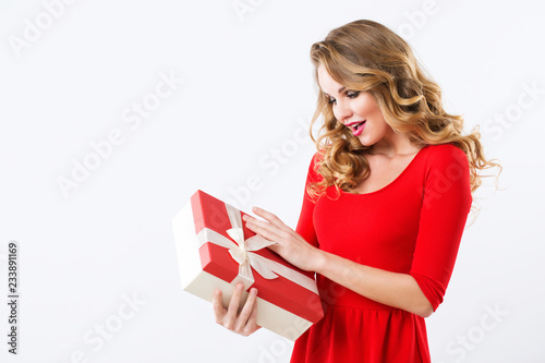 Beautiful cheerful woman in red dress with a gift over white.