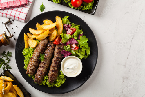 Traditional cevapcici served with baked potatoes. Flat lay. Stone background. photo