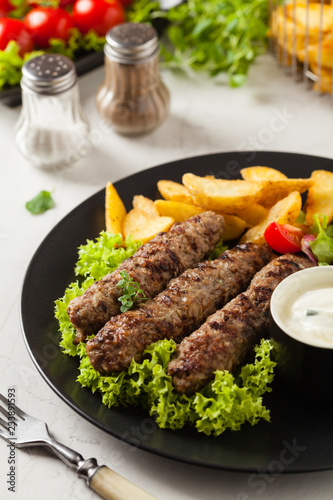 Traditional cevapcici served with baked potatoes. Stone background.