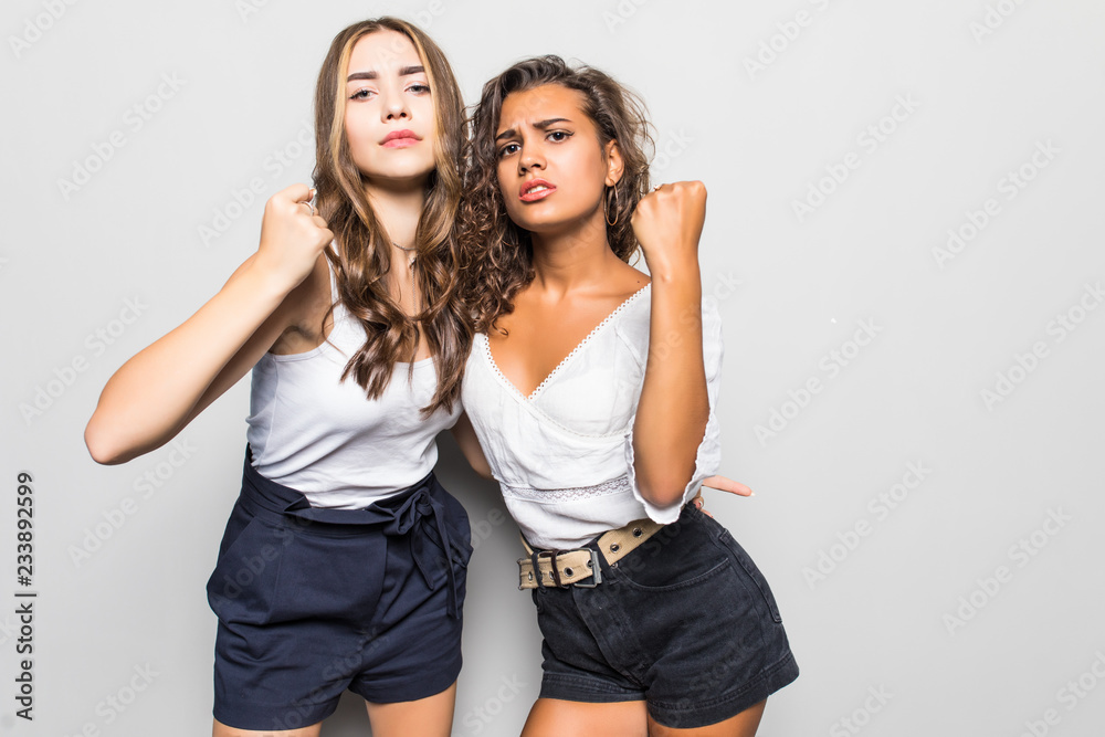 Two angry mixed race women hugging to each other while showing their fists and looking at the camera over gray background Two angry mixed race women hugging to each other while showing their fists and looking at the camera over gray background