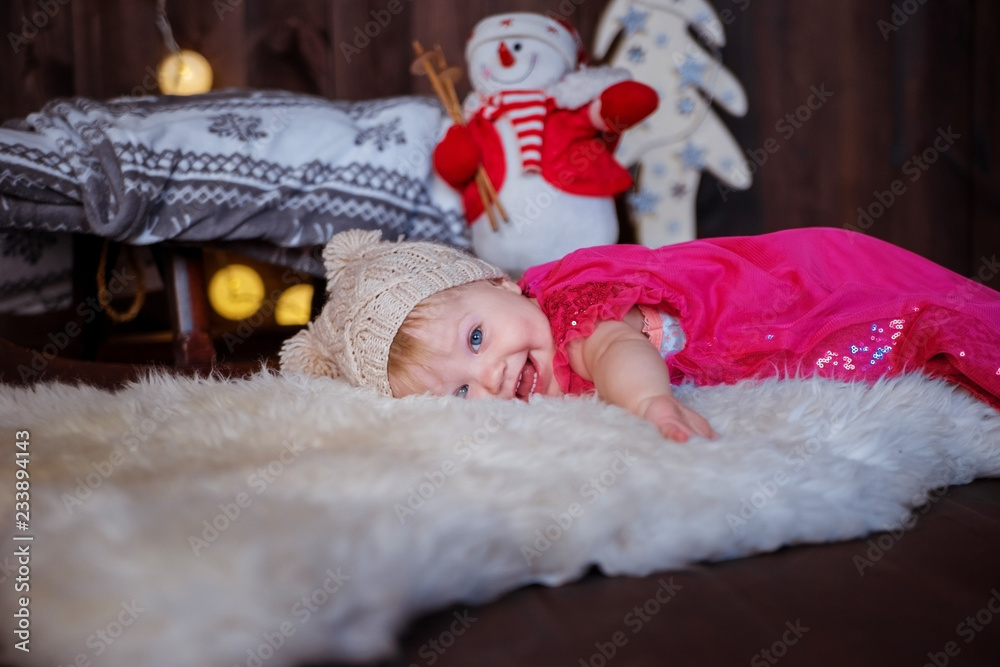 Obraz premium Funny baby girl lying on the carpet in the interior decorated for Christmas.