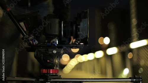 video dslr camera advancing on slider with lights and a fence in background. behind the scenes video production 