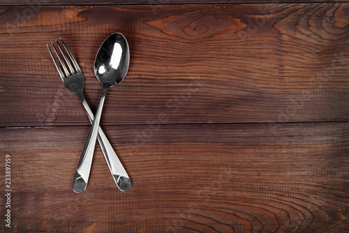 Metal spoon and fork are crossed on wooden background.