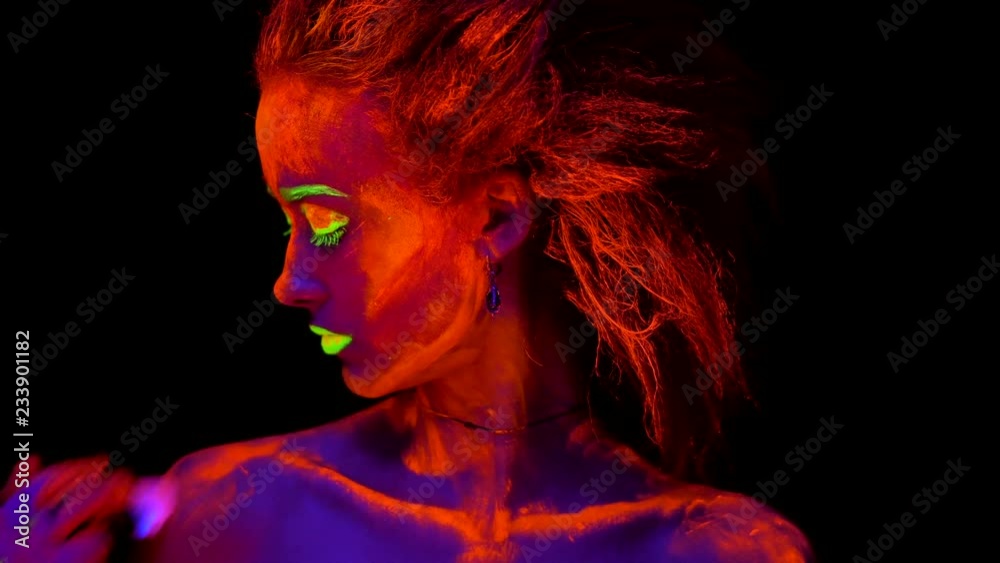 A beautiful young sexy girl with ultraviolet paint on her body looking at a hand of an artist with a brush, painting her shoulder. Pretty woman with glowing bodyart in black lamp light. A beautiful young sexy girl with ultraviolet paint on her body looking at a hand of an artist with a brush, painting her shoulder. Pretty woman with glowing bodyart in black lamp light.