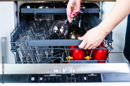 Woman's hand with an open dishwasher filled with clean dishes.