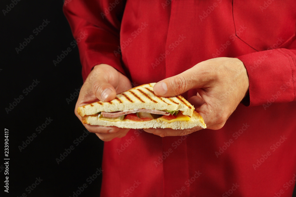 Hands of man in a red shirt with a tasty sandwich on a black background close up