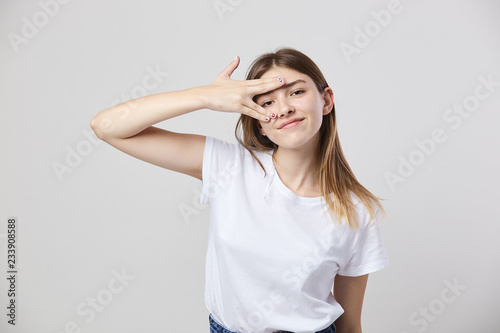 Cheerful and calm girl dressed in a white t-shirt and jeans puts fingers on the face on a white background in the studio