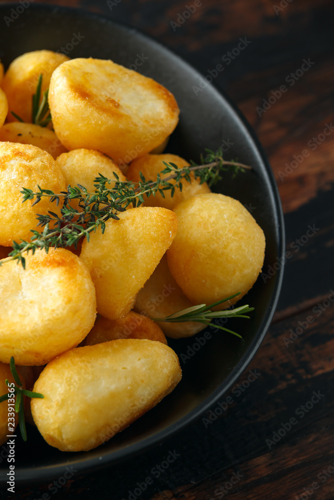 Roast golden potatoes seasoned with salt, garlic, rosemary and thyme on rustic wooden background Roast golden potatoes seasoned with salt, garlic, rosemary and thyme on rustic wooden background
