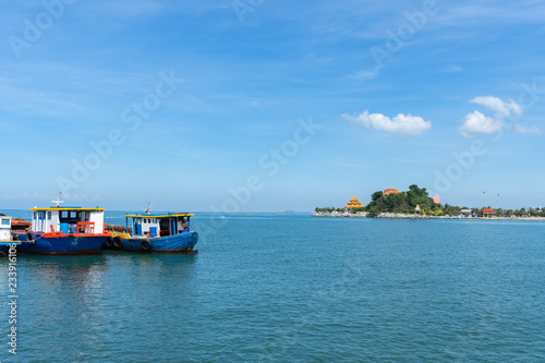 The view of the small island in the distance with the sea and the clear sky with fog with red fishing boat sailing in the ocean.