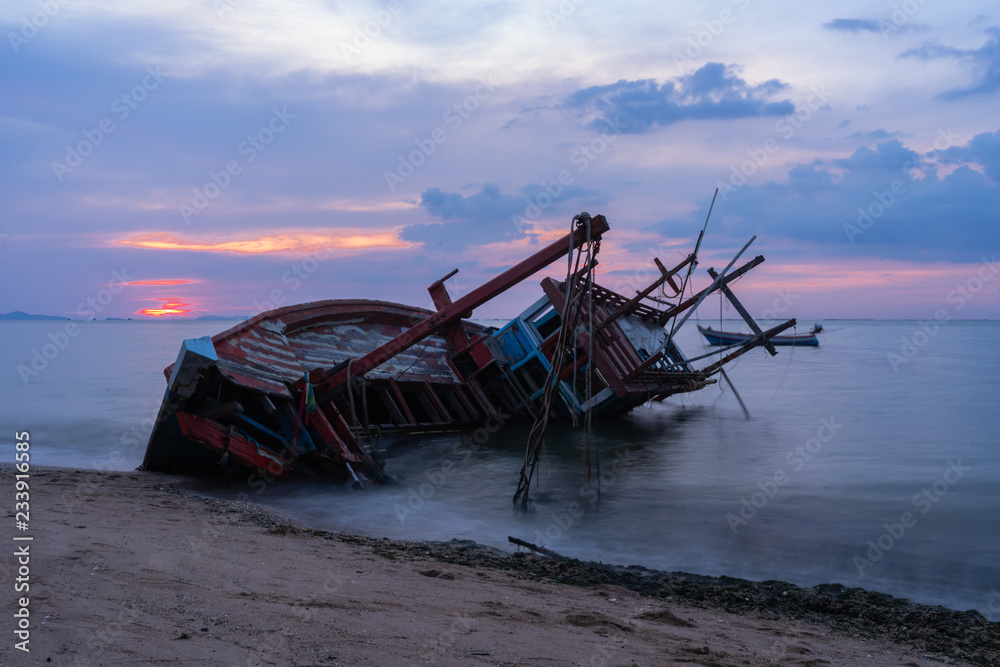 Old fishing boat shipwrecks disposed on the beaches of the eastern coast of Thailand, view and landscape of the sea on sunset and sand with cloud sky.