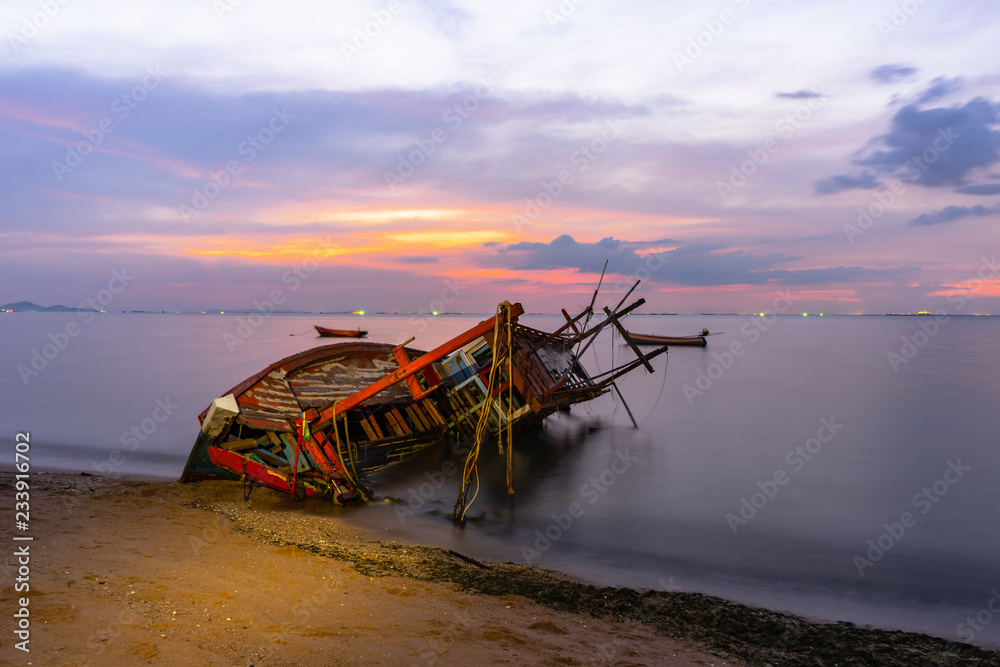 Old fishing boat shipwrecks disposed on the beaches of the eastern coast of Thailand, view and landscape of the sea on sunset and sand with cloud sky.