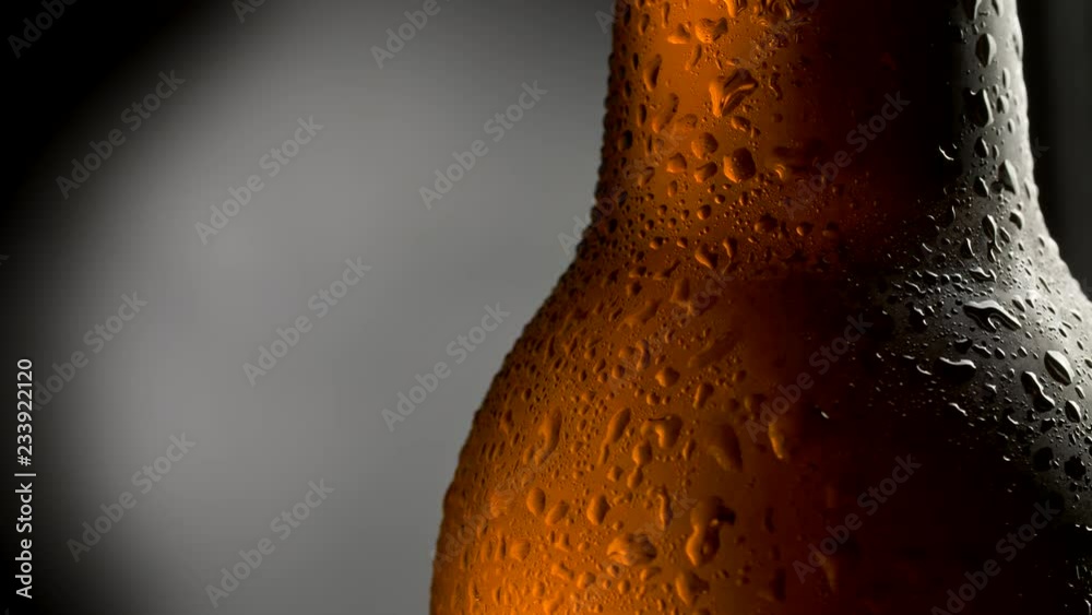 Cold beer bottle with water drops. Close up shot of beer over dark background with rotation. UHD 4K