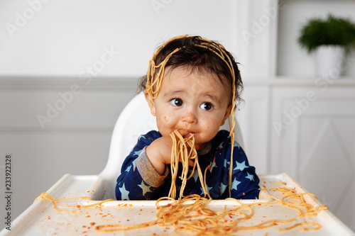 Cute messy baby eating spaghetti with his hands photo