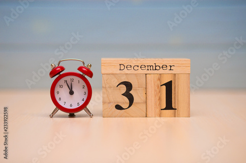 December 31st set on wooden calendar and red alarm clock with blue background.