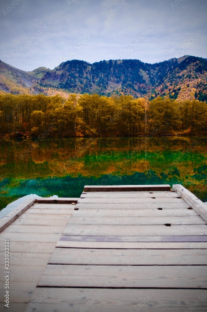 Fototapeta premium Natural landscape view of the autumn red-orange color forest with the reflection on the lake surface