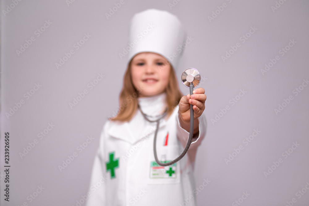 Smiling little girl in medical uniform holding stethoscope and looking at camera isolated