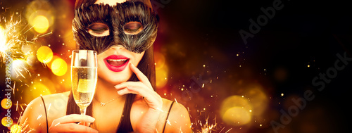 Christmas and New Year holiday celebration. Beauty woman celebrating with champagne, wearing carnival mask. Party, drinking champagne over holiday glowing background