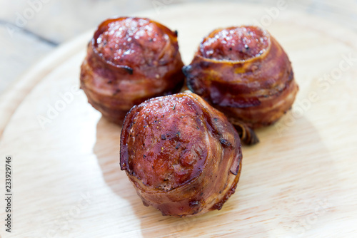 Three meatballs and covered with bacon on cutting board