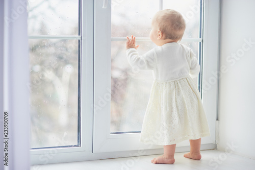 blonde curly toddler Baby girl looking through a window.