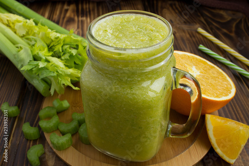 Smoothies with orange and celery on the brown wooden background